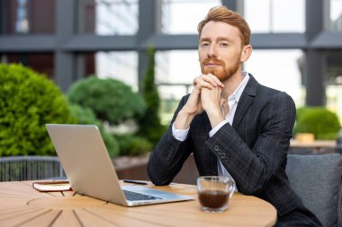 Zencefilli genç işadamı laptopuyla açık kahve masasında güvenle oturuyor.