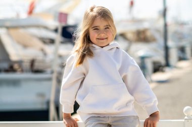 Beyaz kazaklı, çekici sarışın kız yat limanında gülümsüyor.