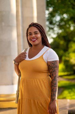 Young woman with braided hair in yellow dress standing near building outdoors in summer
