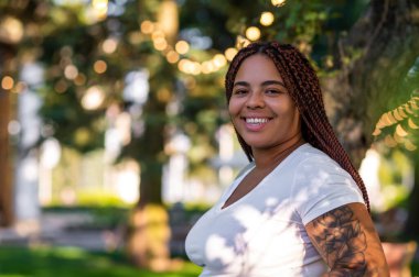 Curvy joyful woman wearing white t-shirt standing outdoors in greenery