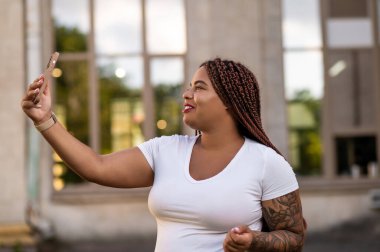 Confident curvy woman taking selfie with smartphone outdoors in city