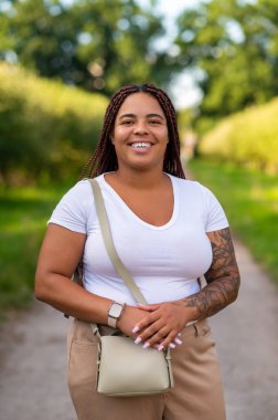 Plus size female model with braids smiling on nature path in summer