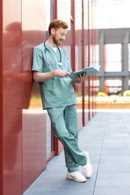Smiling ginger man doctor studying papers in open medical chart