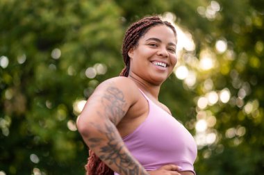 Young African American woman in sportswear posing on outdoor sportsground