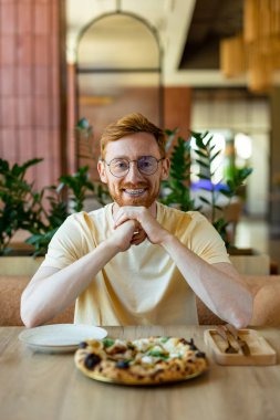 Ginger bearded man in glasses enjoying pizza while dining in cafe