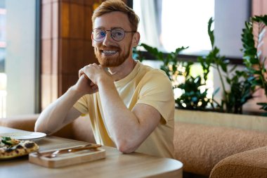 Young adult Caucasian man with ginger hair having lunch with pizza in cozy cafe