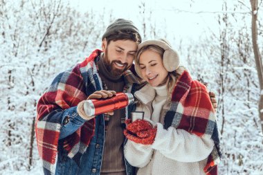 Kış yürüyüşü. Güzel bir çift kış ormanında yürüyüş yaparken sıcak çay içiyor.