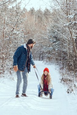 Kızak. Babası kızıyla birlikte kış ormanında kızağını çekiyor.