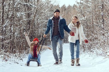 Kış yürüyüşü ve kızak. Genç bir aile kış ormanında yürürken mutlu ve keyifli görünüyor.