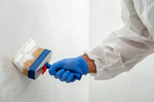 Close-up of the hand of a house painter at work painting a white wall with a paintbrush