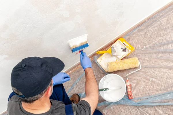 İşçi evi ressam bir boya fırçası ile beyaz bir duvar boyama iş başında