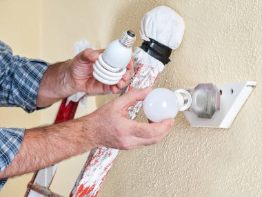 Floresan lamba tavan ışık bir konut elektrik sistemi ile yeni bir Led ampul değiştirmek için elektrikçi teknisyen merdiven üzerinde çalışma.