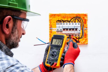 Kask, gözlük ve eller ile elektrikçi teknisyen tarafından korunmaktadır eldiven bir konut elektrik panel gerilim ölçmek.