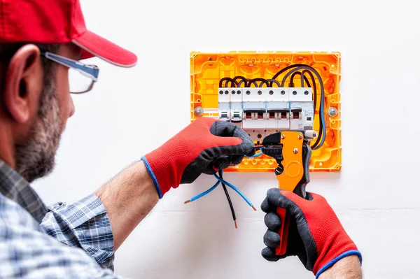 Electrician technician with glove-protected hands, works with the wire-cutter pliers in a residential electrical panel.