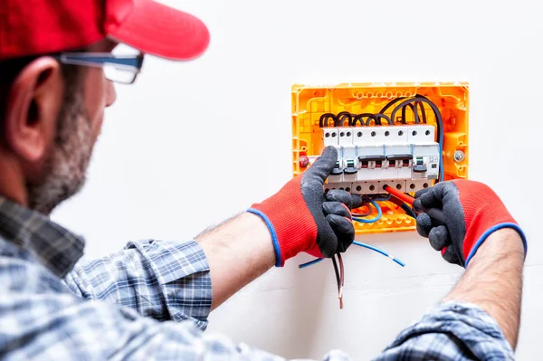 Electrician technician with gloves protected hands, fixes the cable to the switch of a residential electrical panel.