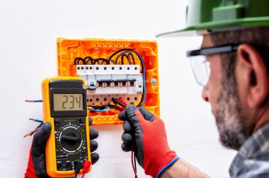 Kask, gözlük ve eller ile elektrikçi teknisyen tarafından korunmaktadır eldiven bir konut elektrik panel gerilim ölçmek.