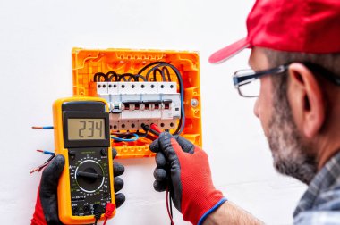 Elektrikçi teknisyen eldivenli elleri korumalı, konut elektrik panelindeki bir gerilim ölçer.