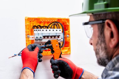 Kask, gözlük ve eldiven ile elektrikçi teknisyen eller, İnşaat Tel striptizci bir konut elektrik panel ile korunan.