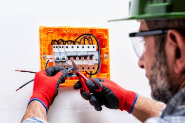 Elektrikçi teknisyen kask, gözlük ve eldiven tarafından korunan elleri ile bir konut elektrik panel kablo ile profesyonel makas keser..