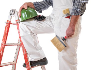 House painter worker on the ladder with white work overalls, keeps the brush for painting in his hand. Equipped with shoes, helmet and protective gloves. Isolated on white background.