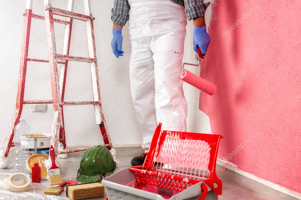 Caucasian house painter worker in white work overalls, with the roller painting the wall with colorful painting. Construction industry.