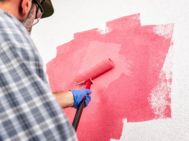 Beyaz Saray ressam işçisi kask ve gözlük, silindir ile o pembe renkli boyama duvar boyar. İnşaat sektöründe. Alt görünümü