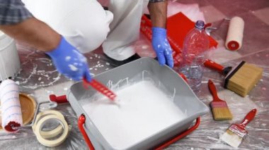 Beyaz Tulum içinde Kafkas ev ressam işçisi, silindir ile duvar boyamak için beyaz boya hazırlar. İnşaat endüstrisi. Görüntü.