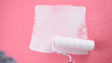 Beyaz Tulum içinde Kafkas ev ressam işçisi, rulo ile beyaz boya ile pembe duvar boyar. İnşaat endüstrisi. Görüntü.