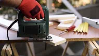 Yetişkin zanaatkar marangoz elleriyle eldivenlerle korunuyor elektrikli testere ile ahşap bir masa kesiyor. Ev işi, kendin yap. Görüntü.