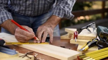 Yetişkin marangoz ölçüyü alıyor ve marangozun karesi ile ahşap bir masanın üzerindeki kesik çizgisini takip ediyor. İnşaat endüstrisi, ev işi, kendin yap. Görüntü.