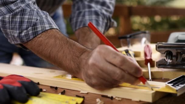 大人の大工職人が対策を取り 大工の正方形で木製のテーブルの上に切断ラインをトレースします 建設業 家事は自分でやる 映像スローモーション — ストック動画