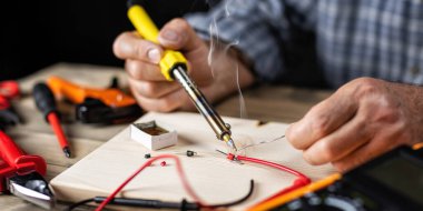 Elektrikli lehimleme demiri olan elektrik teknisyeni çoklu sayacı tamir ediyor. İş yerindeki insanlar. Teknoloji.