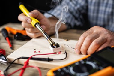 Elektrikli lehimleme demiri olan elektrik teknisyeni çoklu sayacı tamir ediyor. İş yerindeki insanlar. Teknoloji.