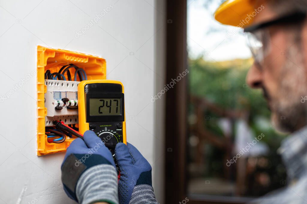 Electrician at work with the tester measures the voltage in the electrical panel of a residential installation. Construction industry. 