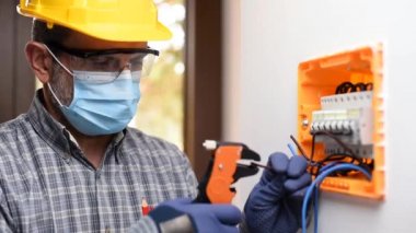 Kask, güvenlik gözlükleri ve eldivenlerle korunan bir elektrik paneli üzerinde çalışan elektrikçi Coronavirus 'un yayılmasını önlemek için cerrahi maske takıyor. İnşaat endüstrisi. Covid-19 Salgın Önleme. Görüntü.