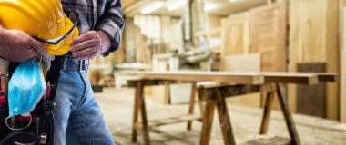 Marangozluk atölyesindeki marangoz, Coronavirus enfeksiyonunu önlemek için kask, gözlük, deri eldiven ve cerrahi maske tutuyor. İş yerinde salgının önlenmesi Covid-19.