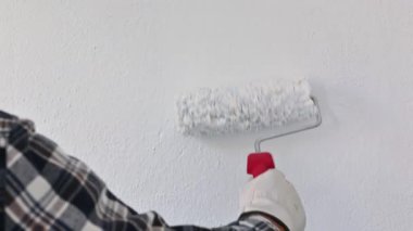Koruyucu eldiven takan ellerin yakın çekimi. Bir ressam rulo kullanarak duvarları beyaz boyayla boyuyor. İnşaat endüstrisi. İş Güvenliği.