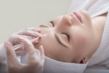 Kozmetik uzmanının elleri yüzüne ve dudaklarına iğne yapıyor. Genç bir kadın güzellik salonunda yüz aşısı yaptırıyor. Yaşlanma, gençleşme ve hidrasyon prosedürleriyle yüzleş. Estetik kozmetoloji. Kapat..