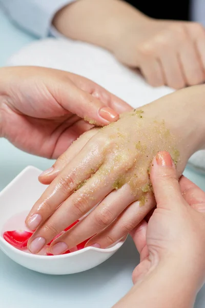 Woman hands in a nail salon receiving a  hand scrub peeling by a beautician. SPA manicure, hand massage  and body care, spa treatments. Close up, shallow dof.