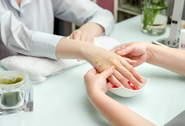 Woman hands in a nail salon receiving a  hand scrub peeling by a beautician. SPA manicure, hand massage  and body care, spa treatments. Close up, shallow dof.