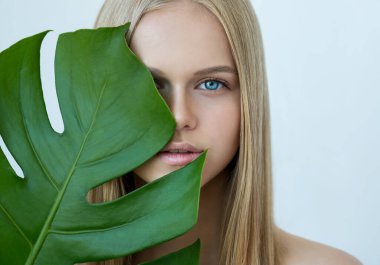 Genç, güzel, gülümseyen, doğal makyajlı, yeşil yapraklı sarışın manken. Spa ve sağlık. Gençlik, gençlik ve cilt bakımı konsepti. Yaklaş, seçici odaklanma.