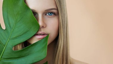 Mükemmel cildi ve doğal makyajı olan tropikal yaprağı olan güzel bir genç kadın. Yeşil yapraklı bir model. SPA, cilt bakımı ve sağlık. 