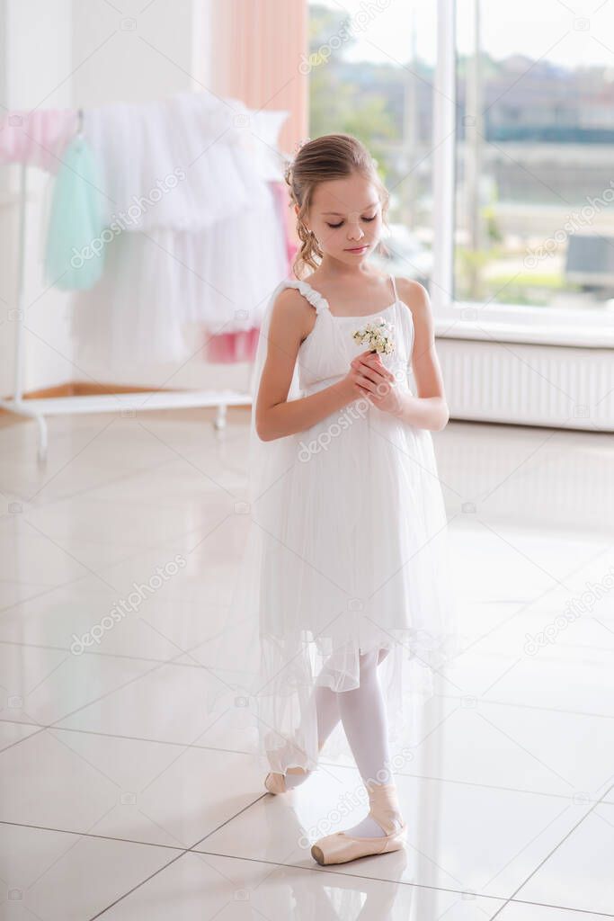 Cute little ballerina in white dress and pointe shoes dreams about ballet dances. Child girl is studying ballet. Kid and dance. Copyspace.