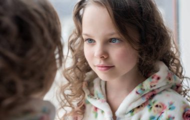 Küçük kız aynadaki yansımasına bak. Güzel küçük bir kızın portresi. Ev banyosundaki aynanın önünde cilt bakımı yaptırıyor. Güzel çocuk yüzünü temizliyor. Gençlik ve çocuk cilt sorunları, hijyen, temiz ve taze cilt.