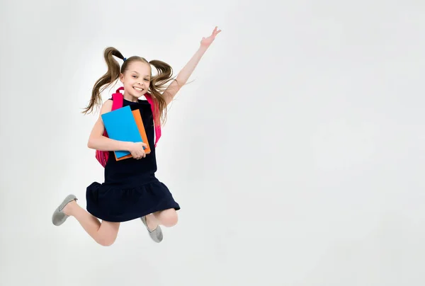 Happy cute child girl in school uniform holding books is jumping. Schoolgirl with facial expression isolated on white. Concept of education, reading, back to school.