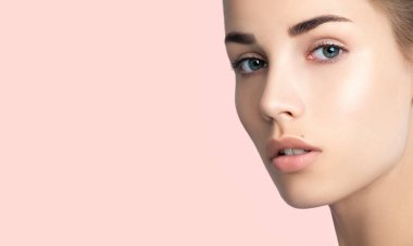 Temiz ciltli güzel genç bir kadının yüzüne yakın çekim. Doğal çıplak makyajlı güzellik modeli portresi. Spa, cilt bakımı ve sağlık. Pembe şeftali rengi mercan arkaplan, kopyalanma alanı.