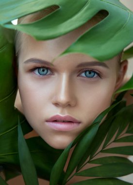 Doğal makyajlı ve yeşil yapraklı güzel, gülümseyen sarışın manken. Gençlik, gençlik ve cilt bakımı konsepti. Spa ve sağlık. Makyaj, uzun saç ve kirpikler. Yaklaş, seçici odaklanma.