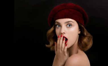 Güzel genç bir kadının portresi kırmızı elbiseler ve bereyle mükemmel genç bir ten, kırmızı dudaklar ve tırnaklar. Koyu arkaplanda parlak kırmızı makyajlı ve manikürlü bir model.