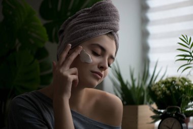 Yüzüne yüz kremi süren genç bir kadın. Mükemmel taze cilde ve uzun kirpiklere sahip güzellik mankeni evde cildini önemser. Spa ve Sağlık, Cilt Bakımı Konsepti. Kapat, seçili odak.