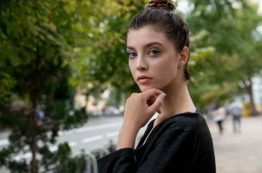 Açık alanda oturan genç ve güzel bir kızın portresi. Doğal makyajlı ve uzun kirpikli güzellik modeli dışarıda gülümsüyor. Kopyalama alanı.